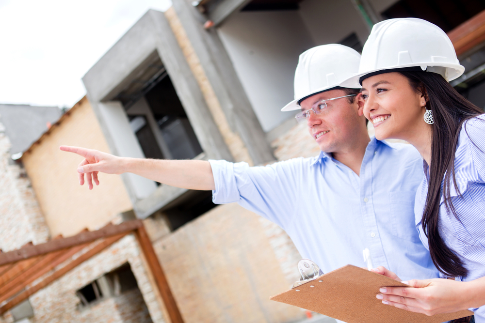 male and female construction worker with hard hats on pointing